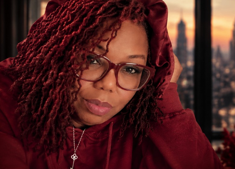 Keysha in a red hoodie and glasses with a city skyline at sunset behind her